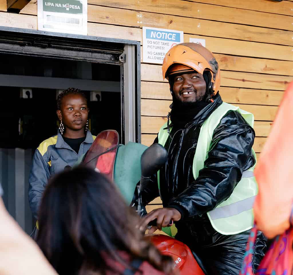 A motorcyclist smiles while idling on an electric motorcycle at an East African Ampersand facility