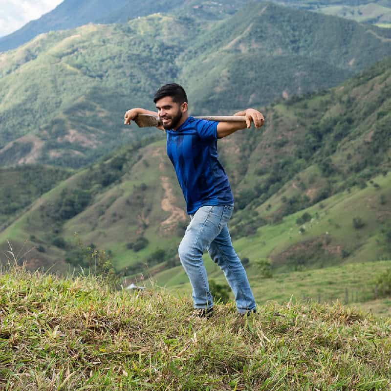 Acumen Fellow Andres Felipe González Espinosa carries a farm tool through a Colombian rural field