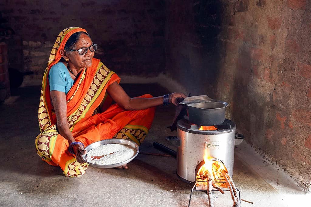 Woman prepares rice on a Greenway Grameen cookstove in a room