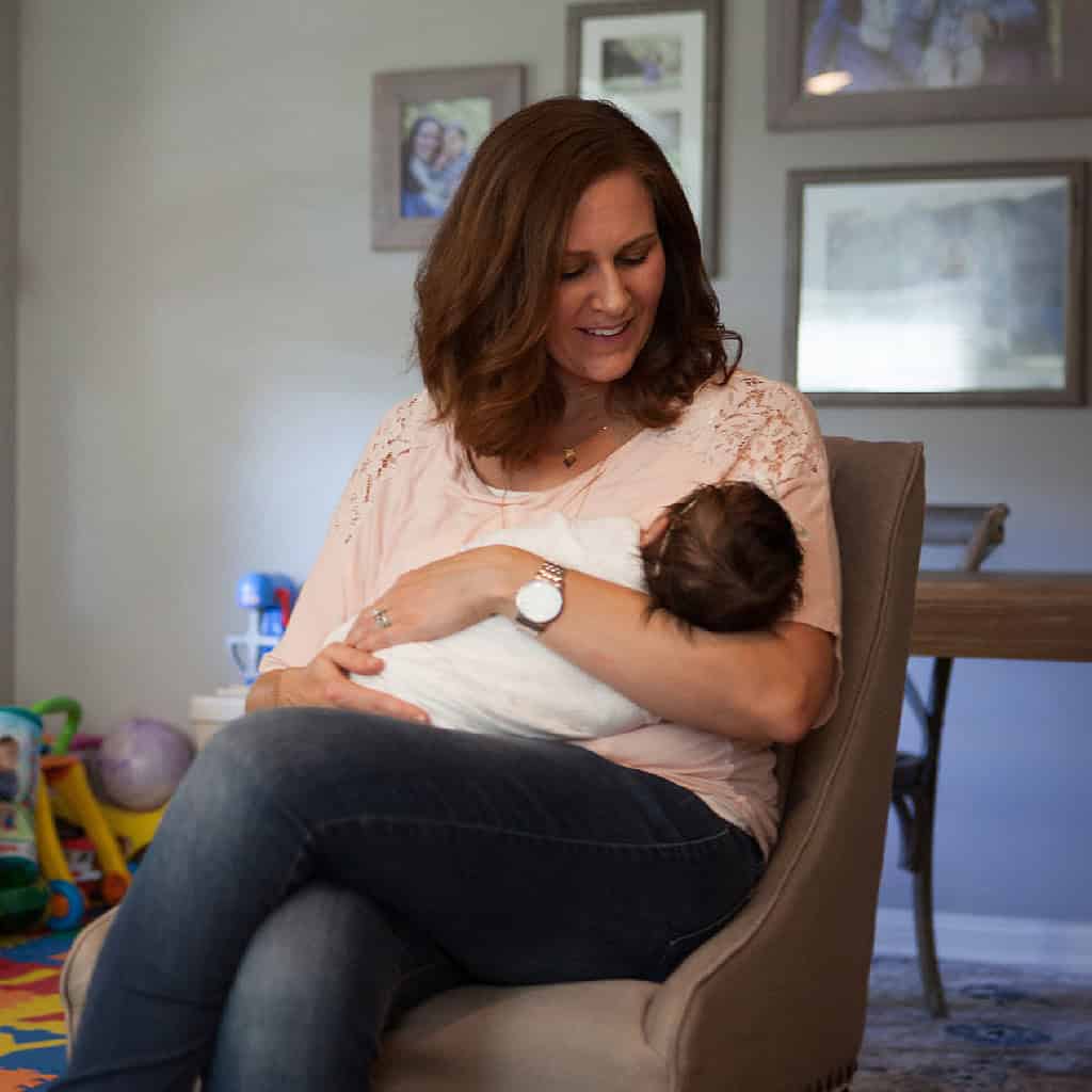 Woman soothes baby while sitting on chair in her living room