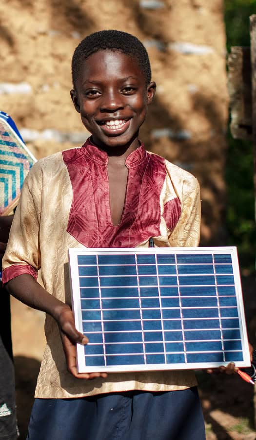 Boy smiles proudly while holding solar panel in West Africa