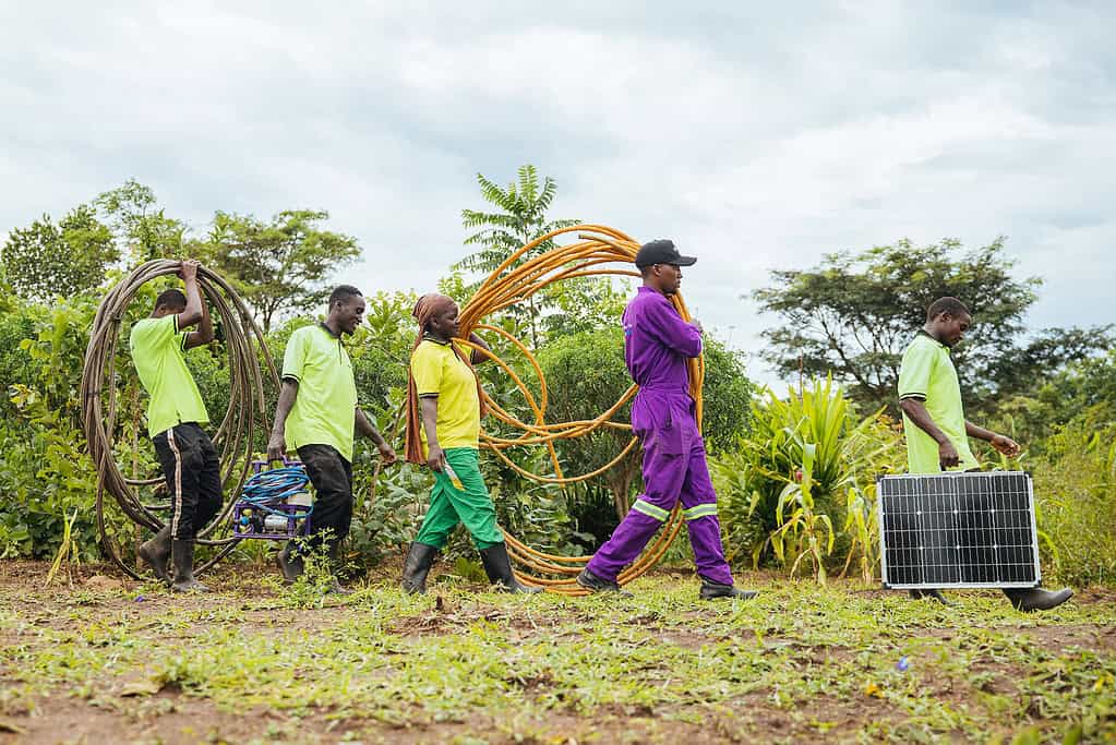 Group of works carry solar energy equipment through a farming field