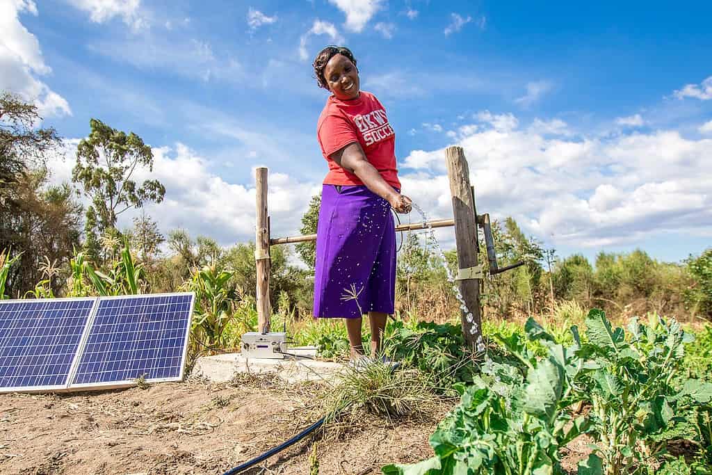 Woman happily waters her garden using a solar powered water pump