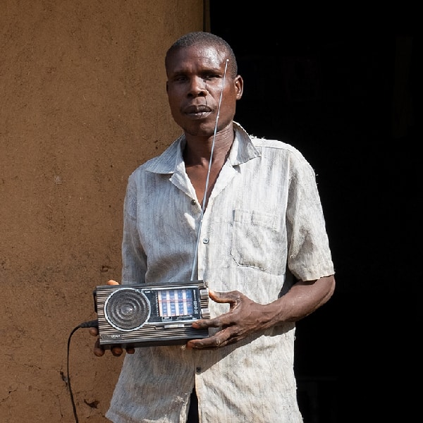 Man stands outside of hut holding a solar-powered radio in Busia, Kenya
