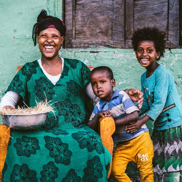 Women and children gleefully laugh in front of their east African home
