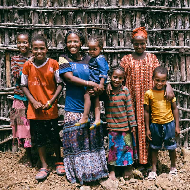 A mother and her several children stand smile against a wooden wall