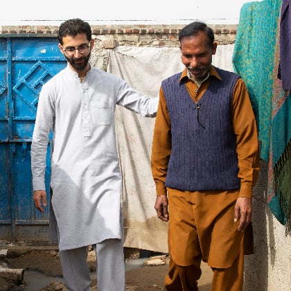 A younger male walks beside an older man in a Pakistani neighborhood.