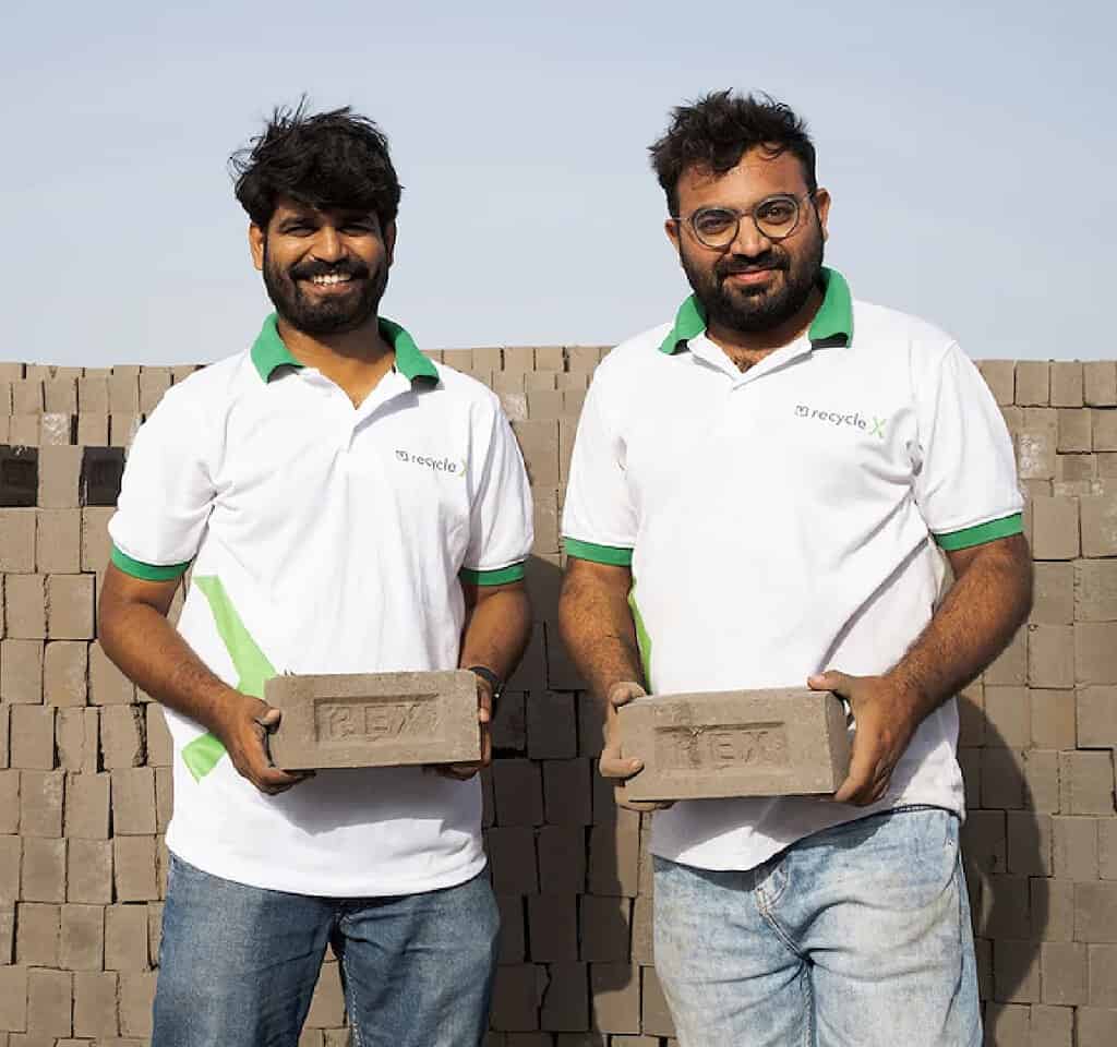 Two men hold up bricks made from recycled materials