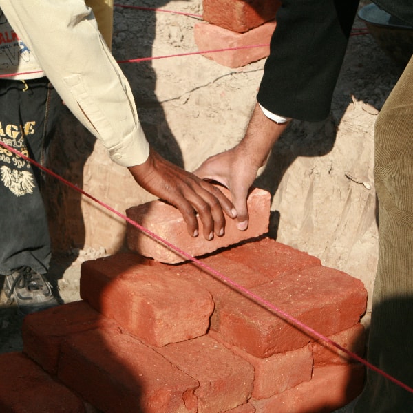 Two hands grab the same brick at a construction site