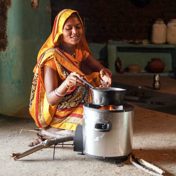 A women warms a cooking pot over a Greenway Grameen clean biomass cookstove in the middle of her home in India