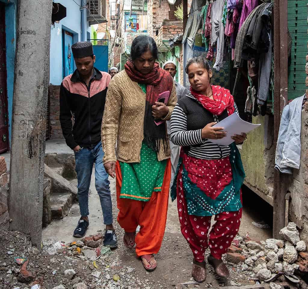 A group of people walk in a tight Indian neighborhood alleyway