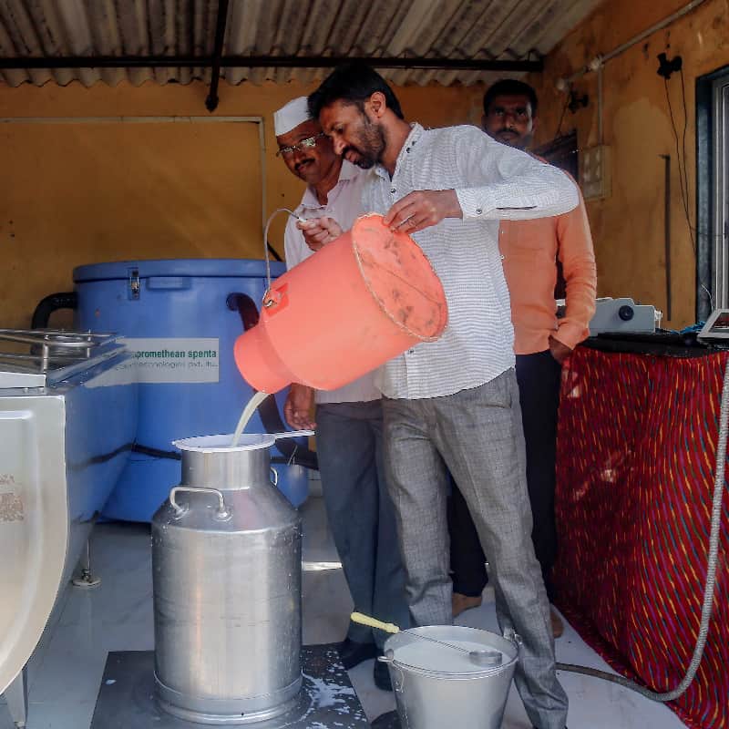 Two men pour milk from one container to a larger container in a Indian processing facility
