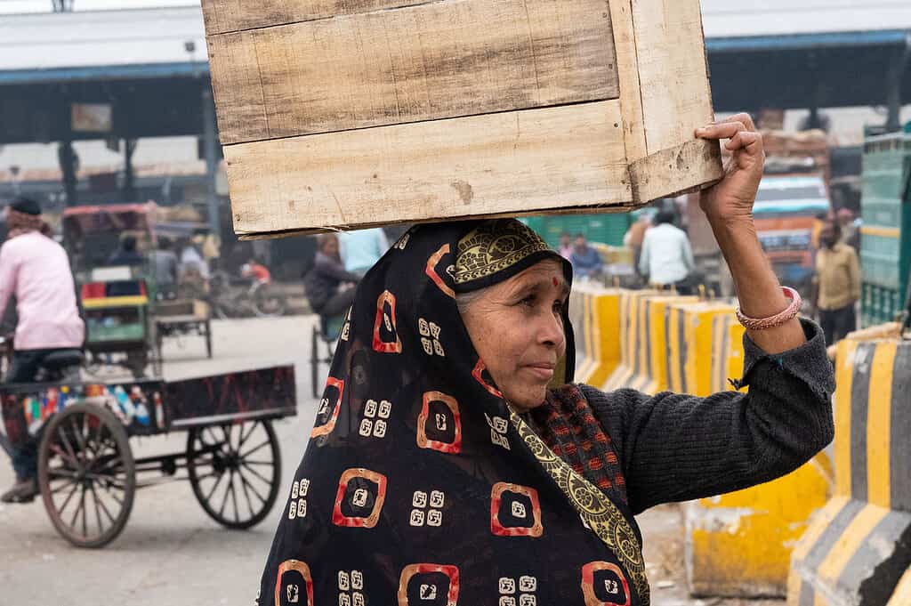 Women carries wooden box on her head across busy Indian road