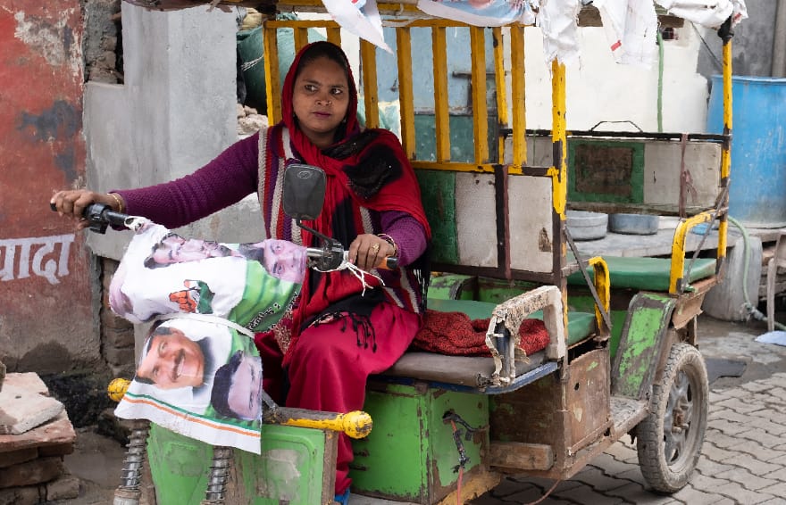 Woman driving a rickshaw, motorbike, through a neighborhood street in India