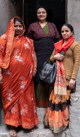 A group of three women stand in the entrance to an alleyway in India