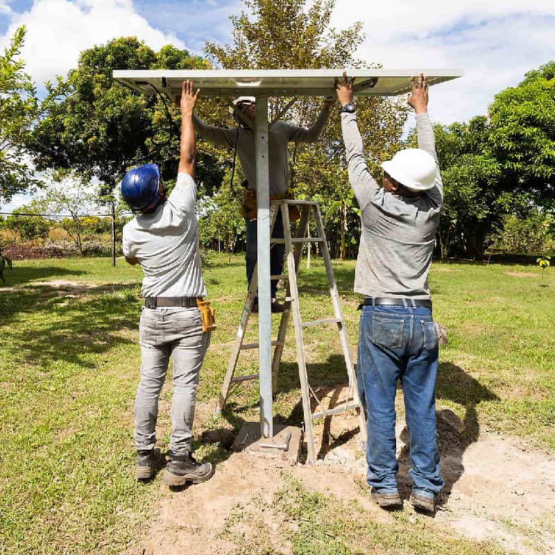 Three technicians carefully install solar panel in a yard at a rural Colombian home