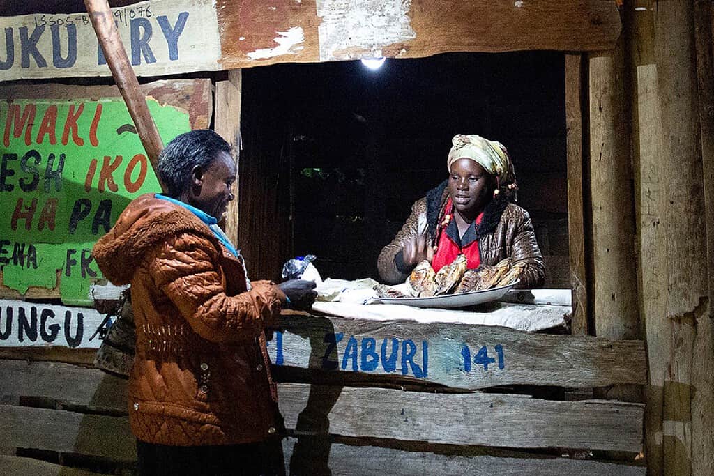 Woman buys fried fish from a shop using solar powered lights