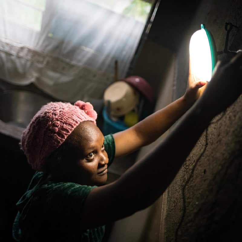Woman hangs solar powered light over her kitchen sink in East Africa