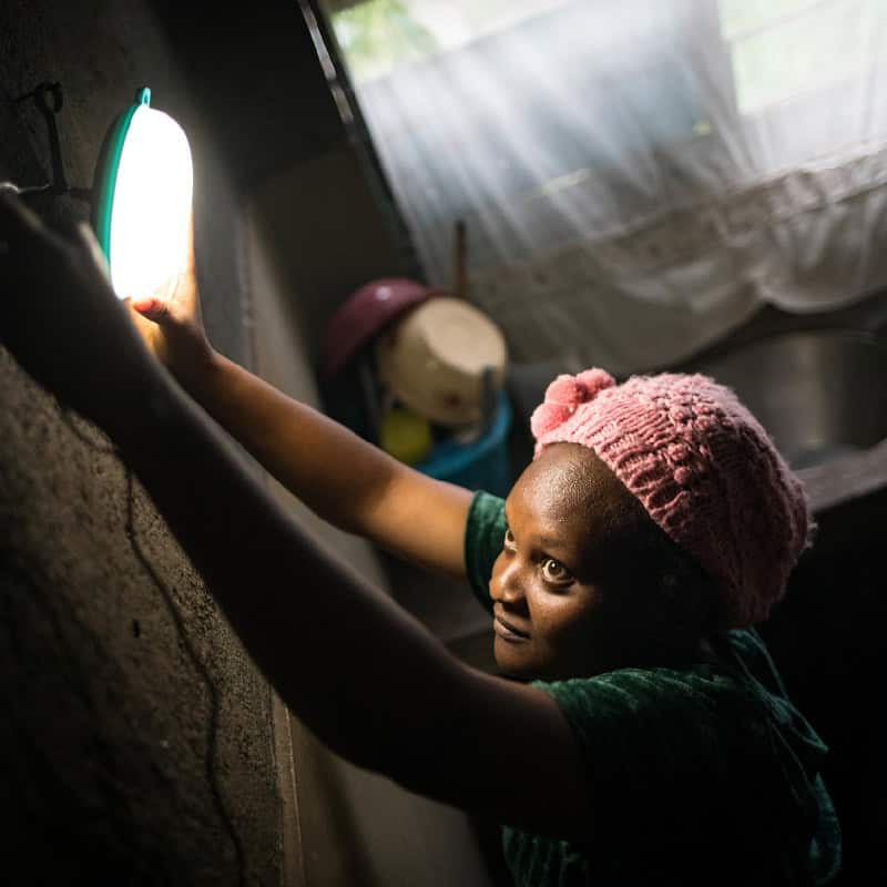 Woman hangs solar powered light over her kitchen sink in East Africa