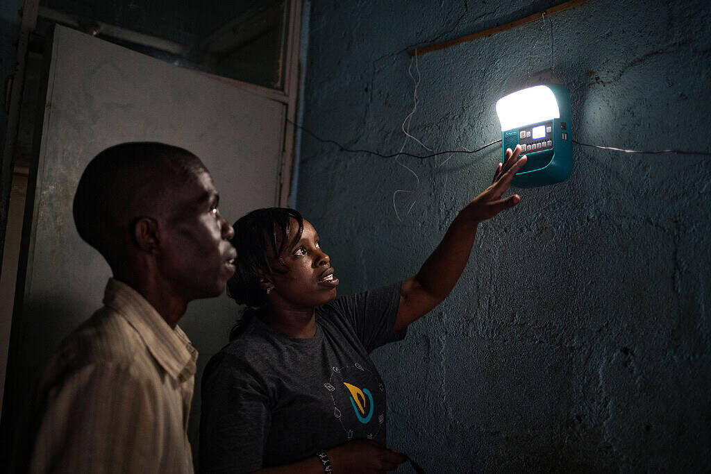 Technician shows man how to operate solar powered lighting in East African home