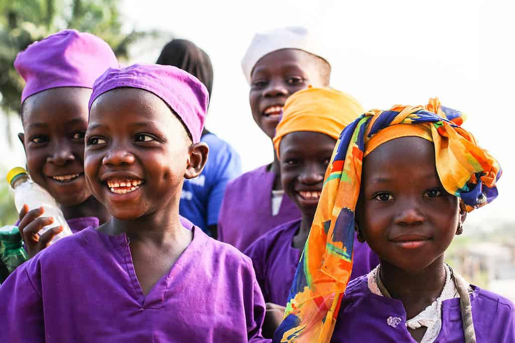 A group of children in school uniforms smile and laugh in the Sierra Leone sun