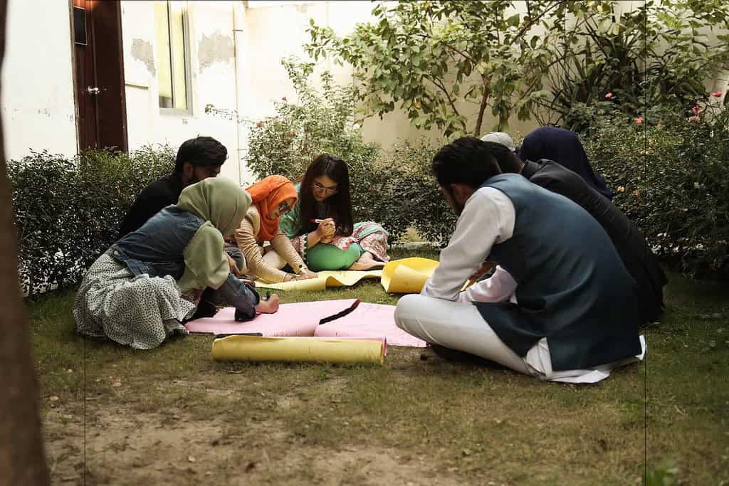 A group of students work on a poster in the garden of a Pakistani school building
