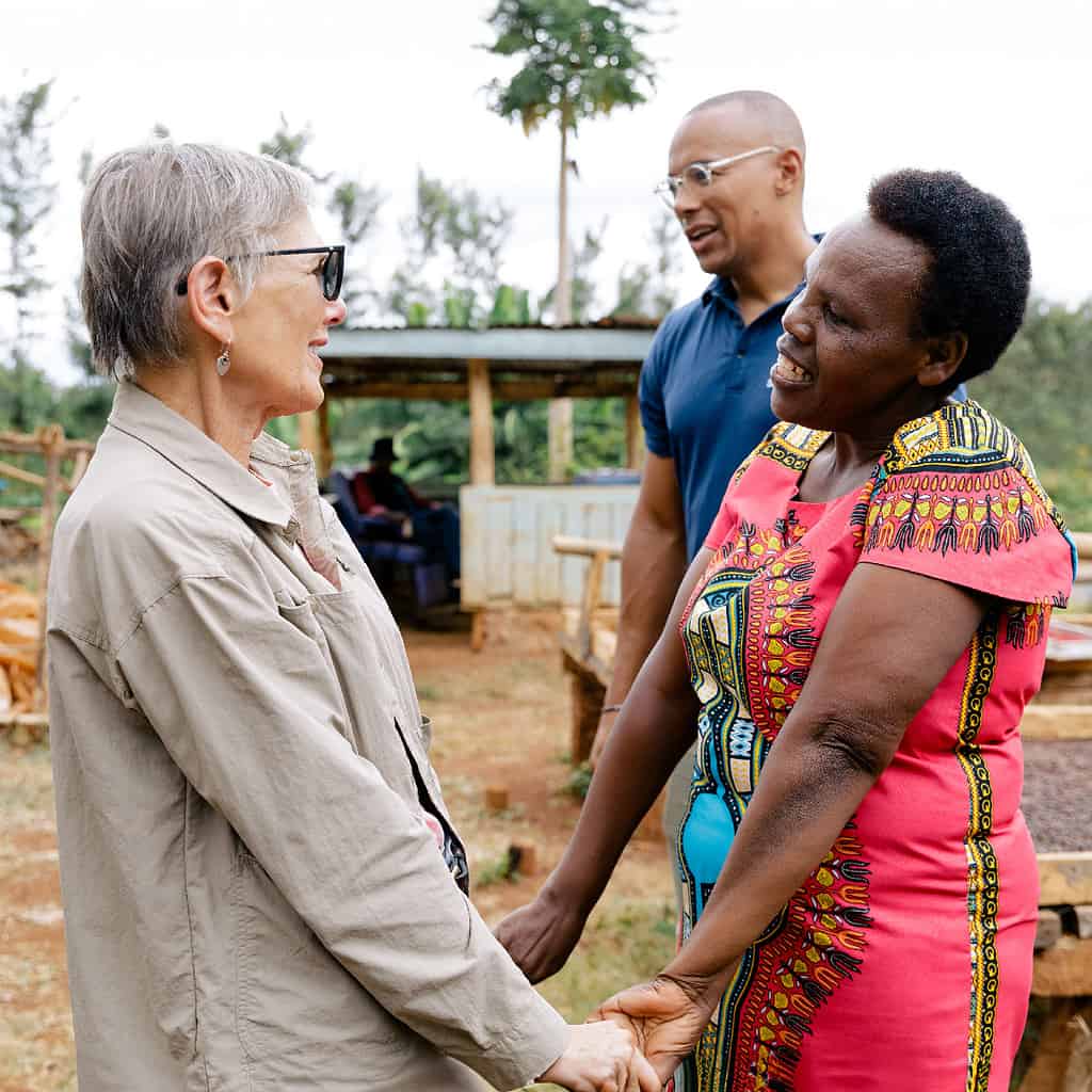 Two women gleefully hold hands while speaking in a African field