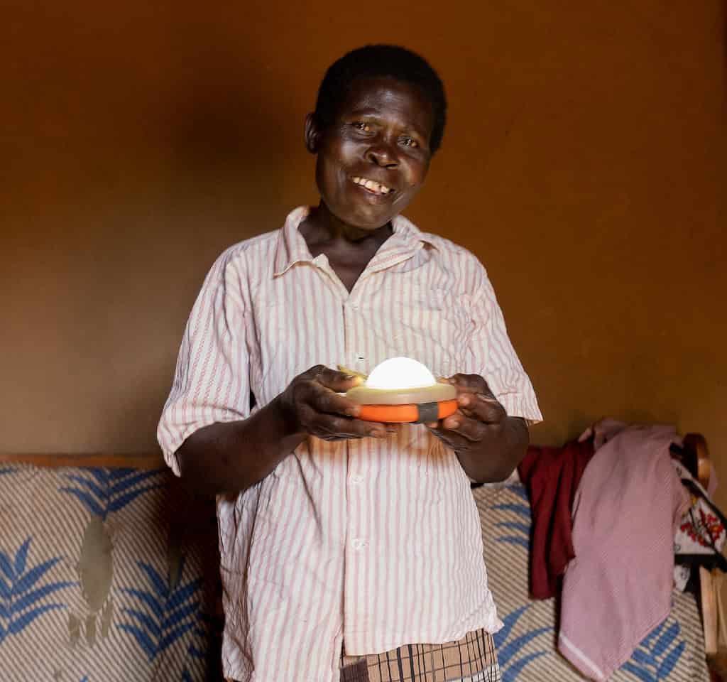 Woman smiles while holding solar powered light in her East African home