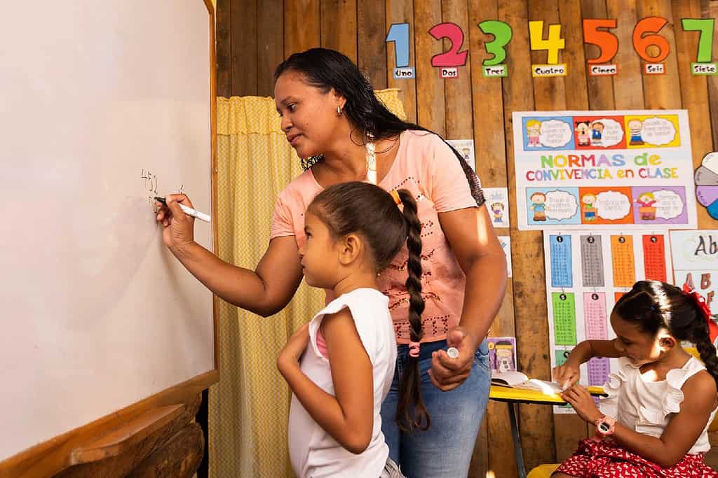 Teacher explains math problem on a white board to child in rural Colombia