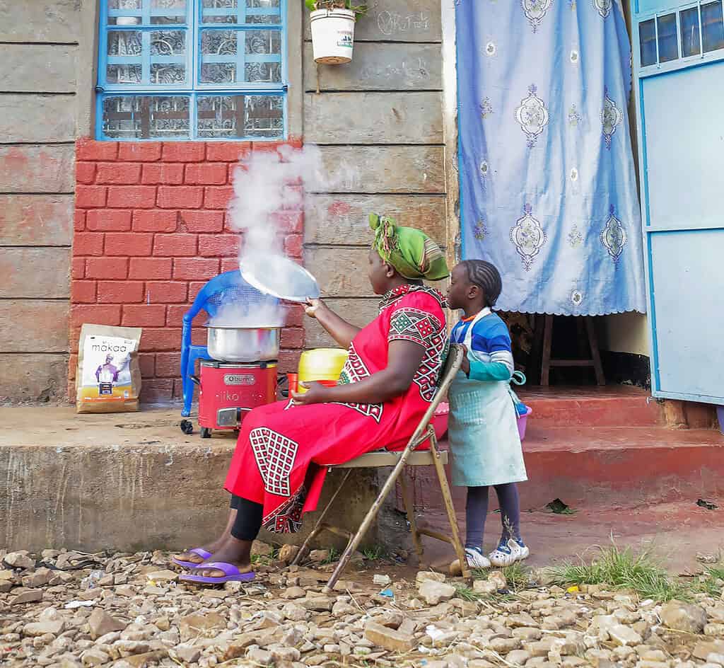A mother cooks using a clean cookstove on her home stoop with her child