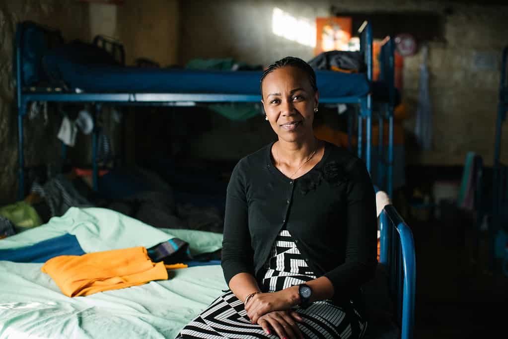 Fellow Teresa Njoroge sits on cot in East African dormitory