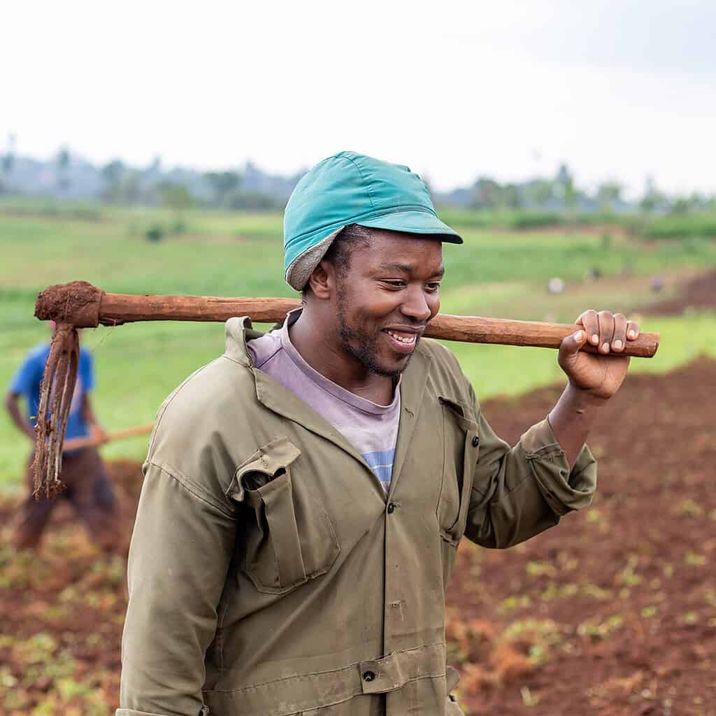 Farmer smile cheerfully while carrying tools and walking through