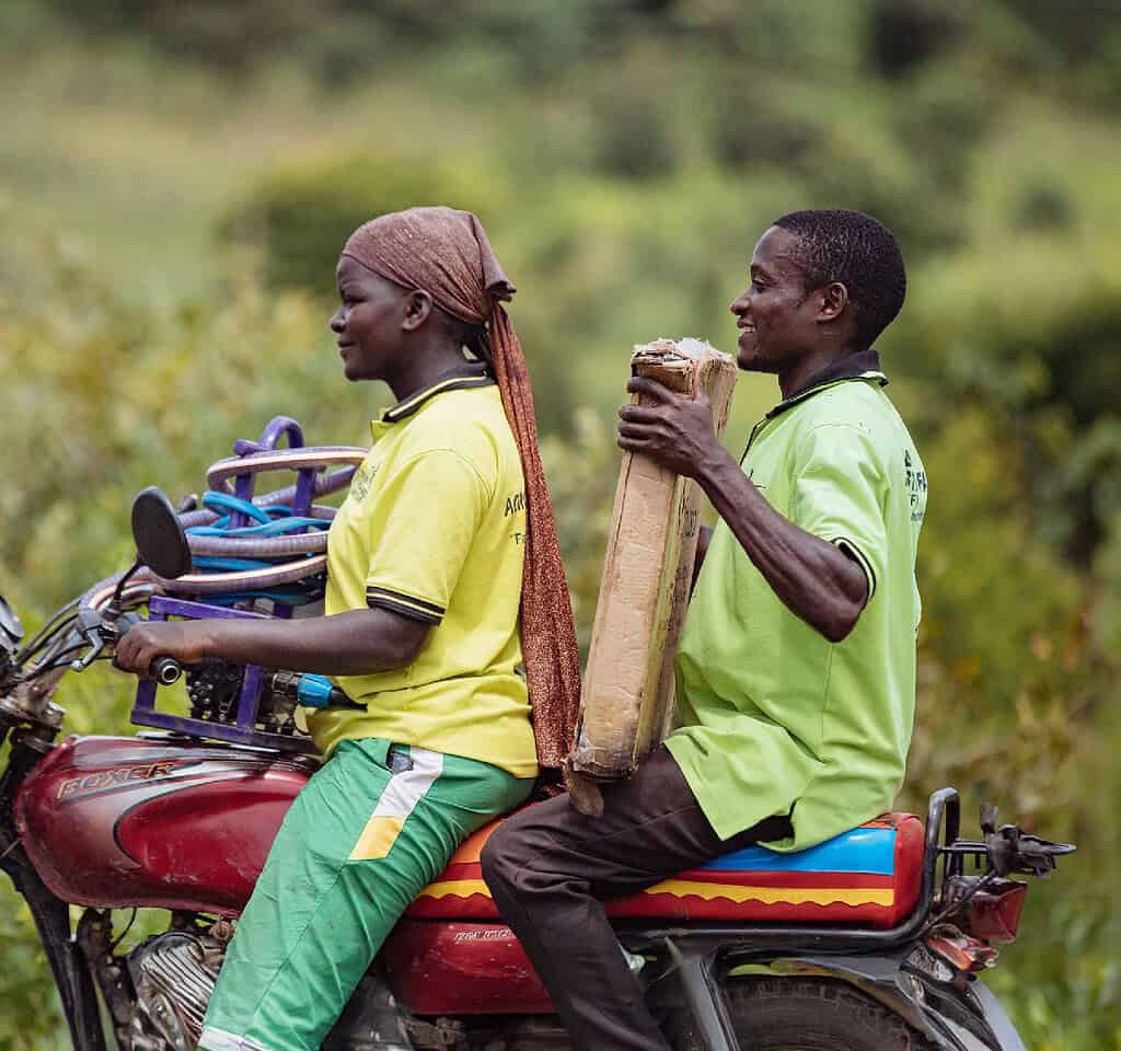 Man and women ride a motorcycle in East Africa while carrying solar panel equipment