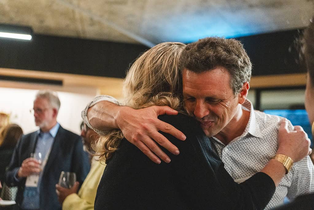 Man and women share a friendly hug at a Acumen event