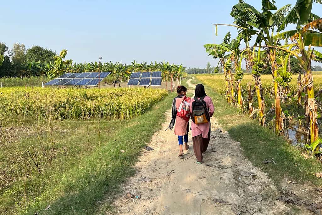 Two women walk through a rural Indian road with solar panels in along side