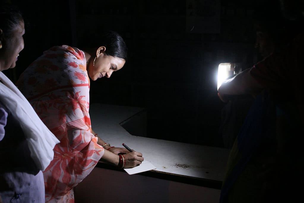 Woman writes in notebook using d.light pay-as-you-go solar powered lantern as a light source