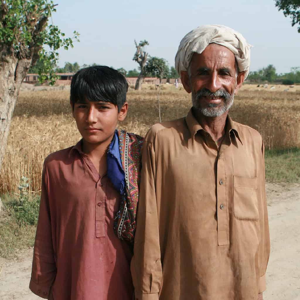 A man and a boy are standing in a rural area with fields and trees.