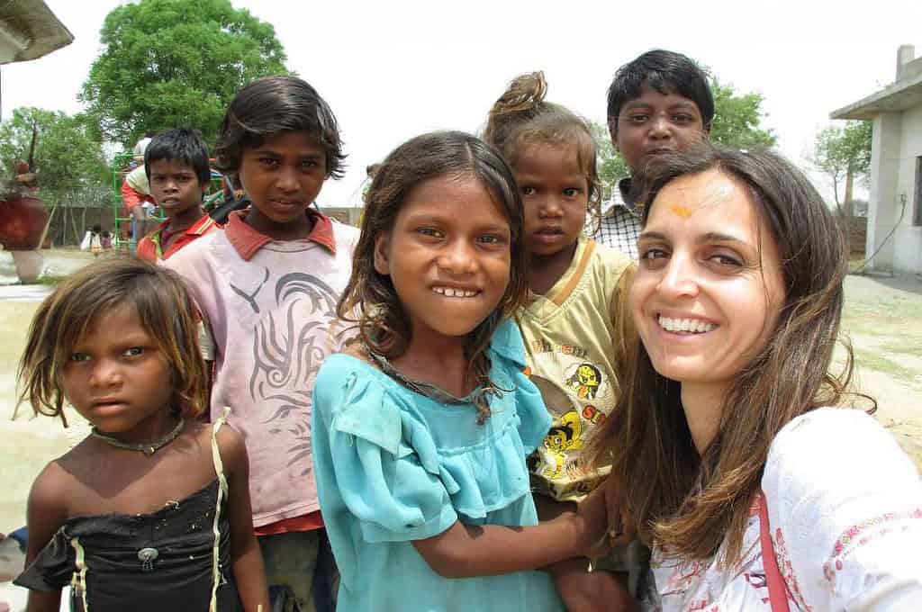 Woman taking a selfie with a group of smiling children outdoors in a rural area.