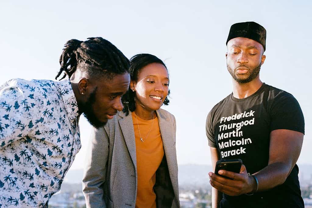 Three young adults look at phone on a clear and sunny day