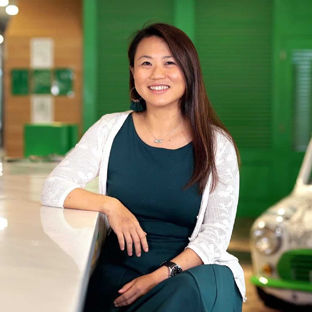 A person is sitting at a counter, smiling, with a green and white background.