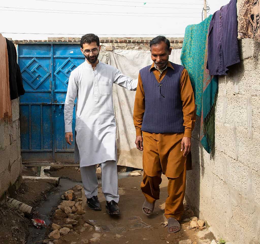A younger male walks beside an older man in a Pakistani neighborhood.