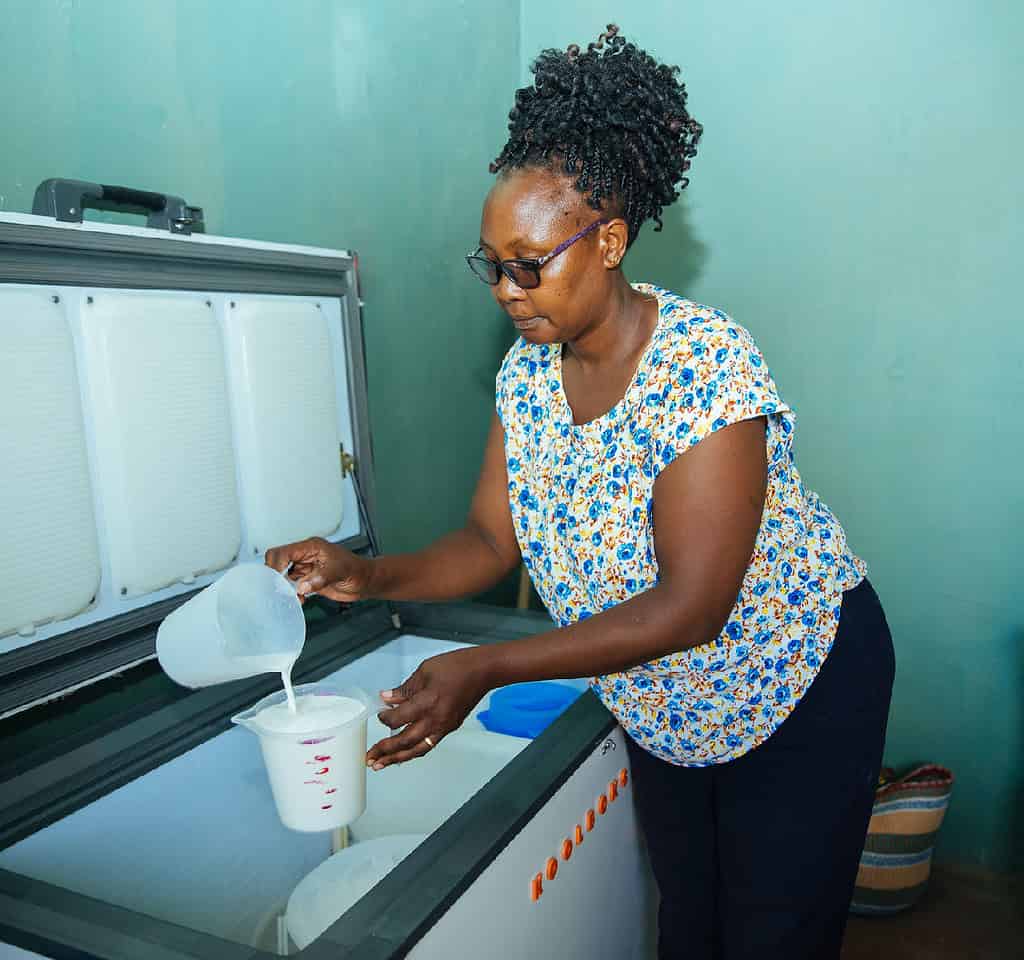 Woman pulls out milk jug and measures portion over a Koolboks refrigerator unit