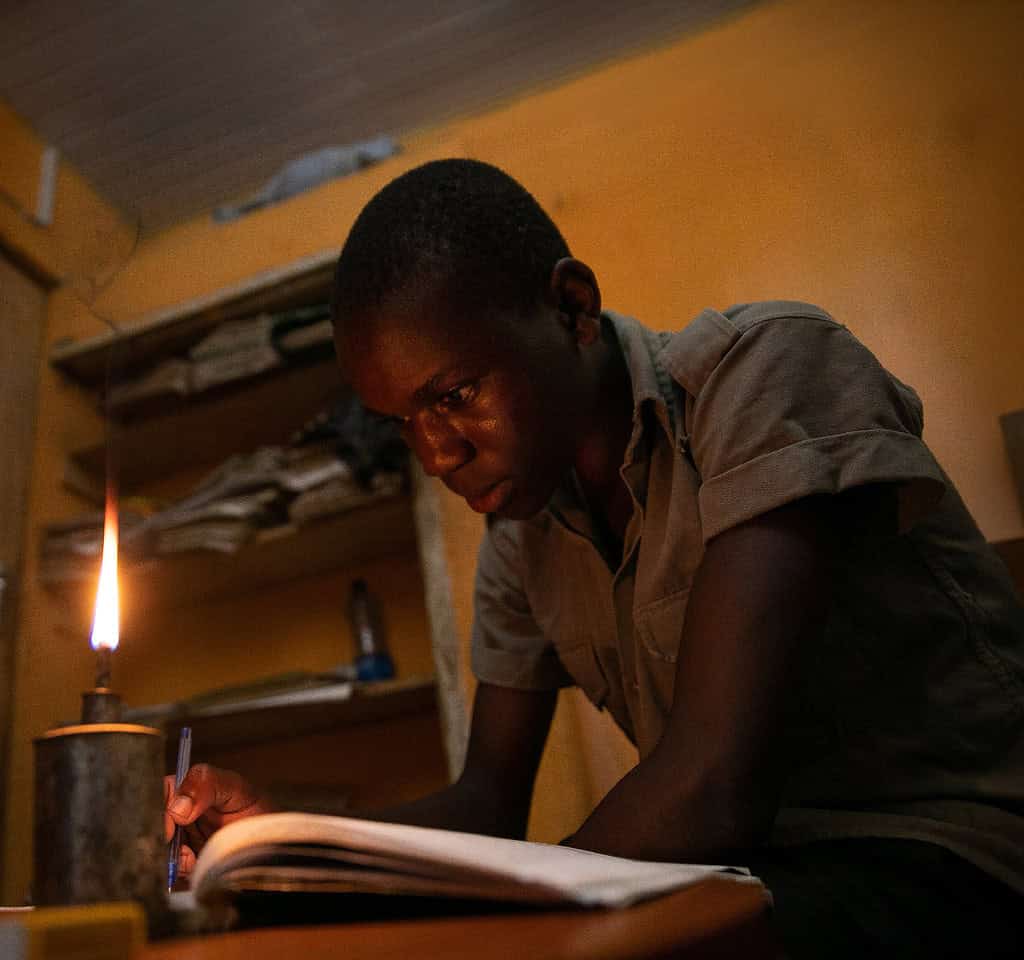 A young man writes in book under oil lamp in East Africa as there is no renewable energy present