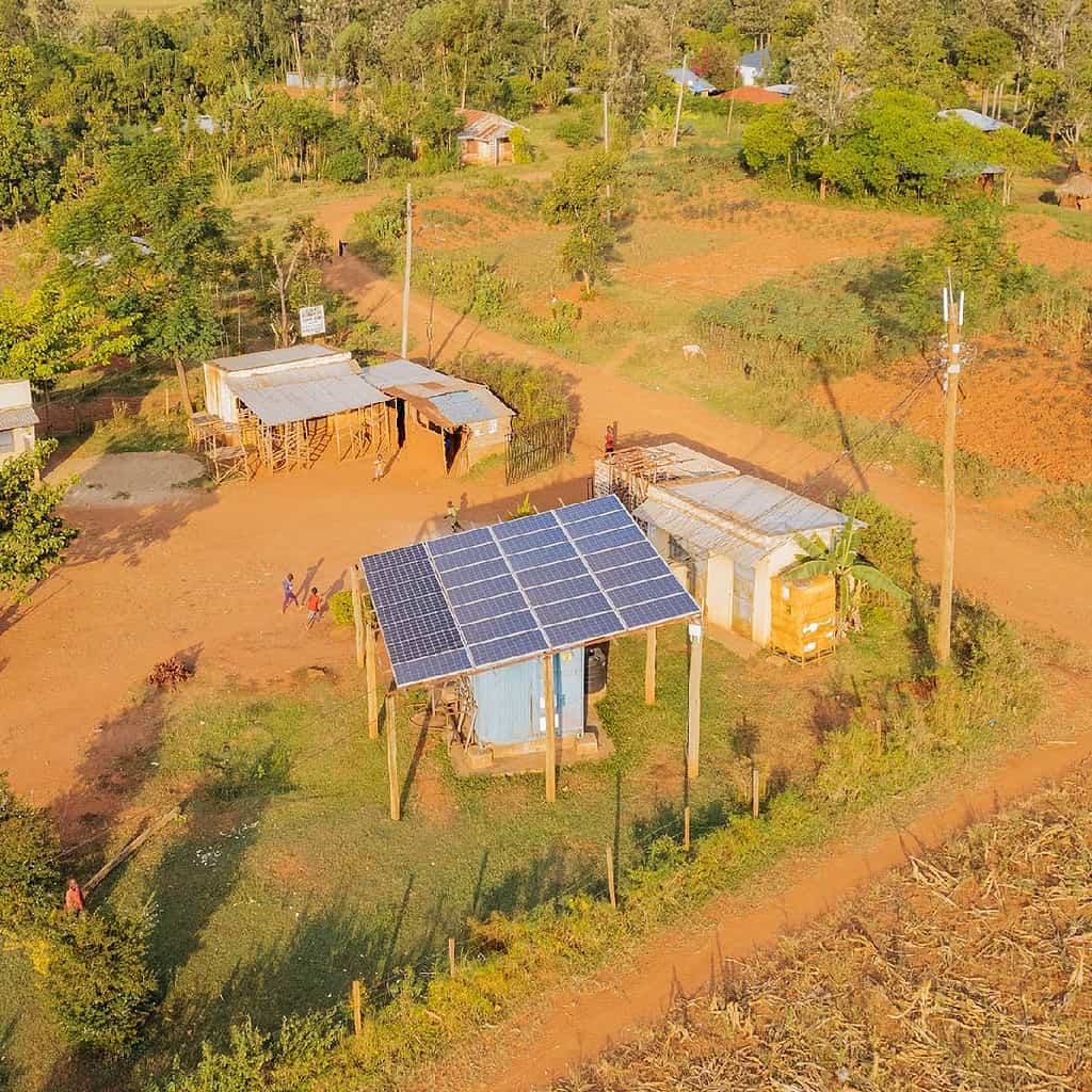 A rural area with solar panels on rooftops, small buildings, and surrounding greenery.