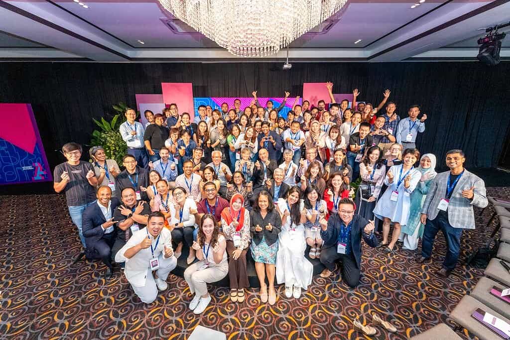 A group of people holding up hand signs such as finger hearts and a thumbs up. Possibly members of Acumen Academy.