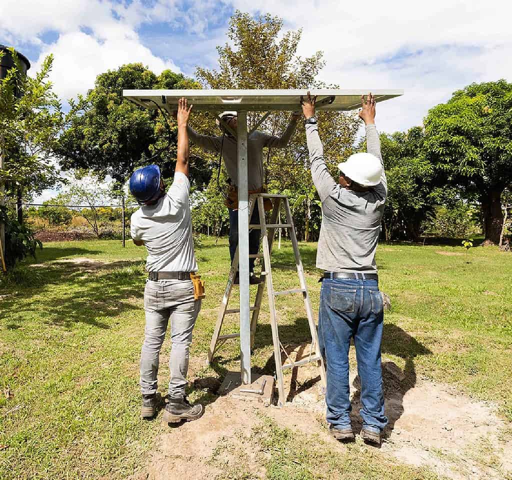 Three technicians carefully install solar panel in a yard at a rural Colombian home