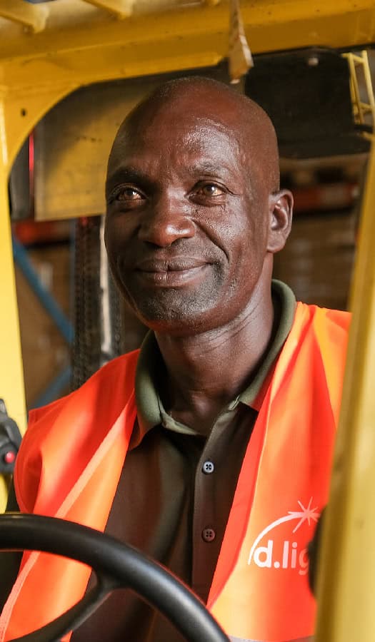 A man in a reflective vest is sitting and smiling, possibly in a vehicle or industrial setting. Sub-Saharan Africa may be relevant.