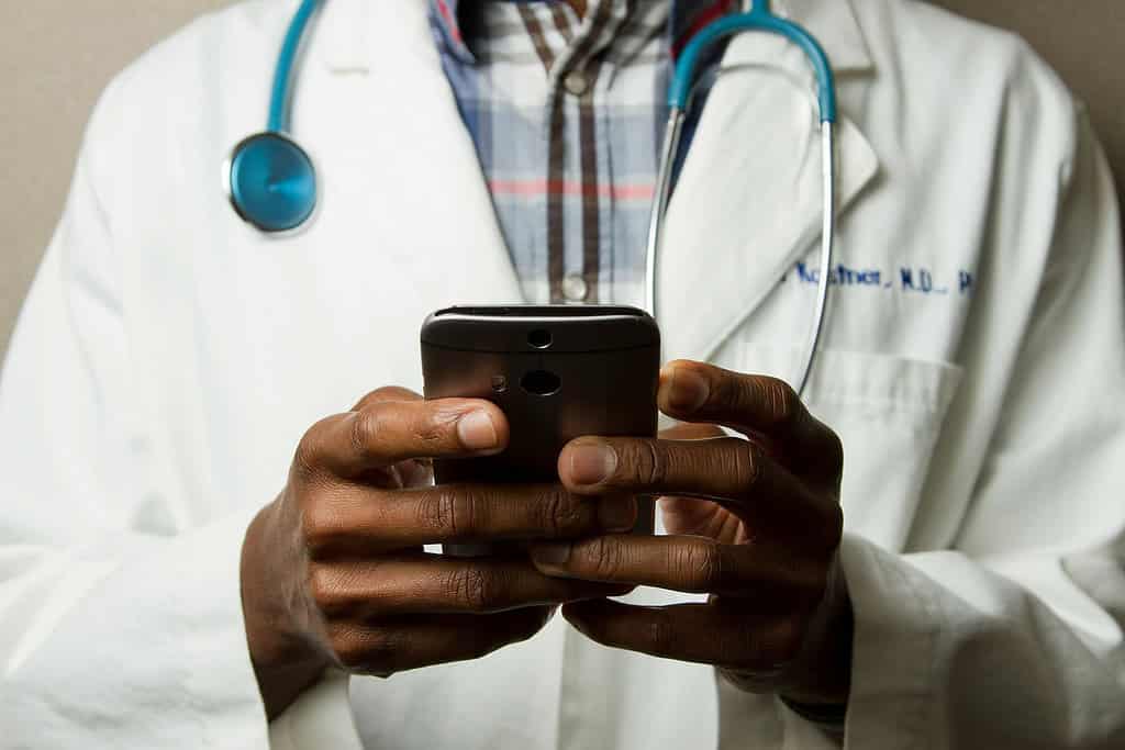 A doctor wearing a stethoscope uses a mobile phone.