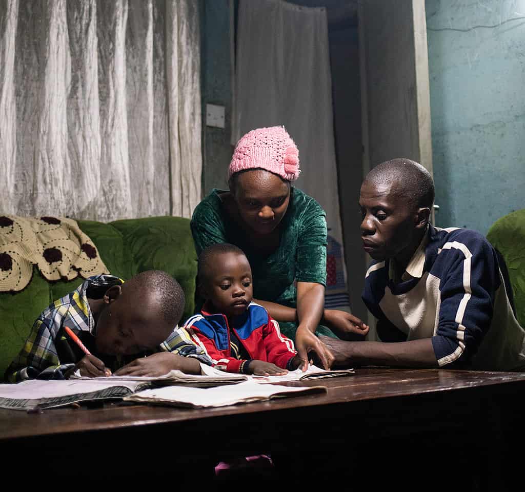 Family sits around table helping children with their homework under solar-powered lighting