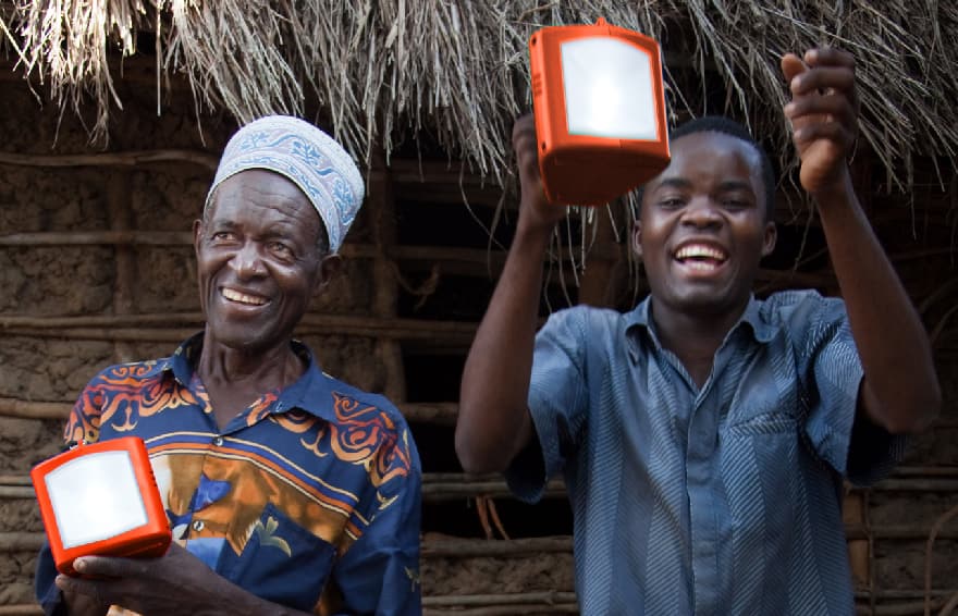 Two men cheerfully and proudly hold solar powered rechargeable lamps